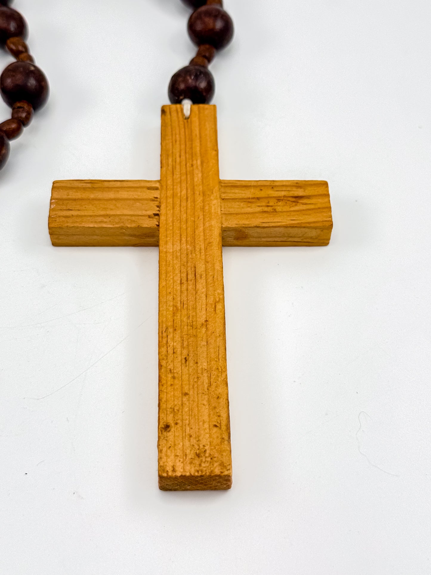 Vintage wood bead rosary coiled on white background showing deep burgundy beads and carved cross