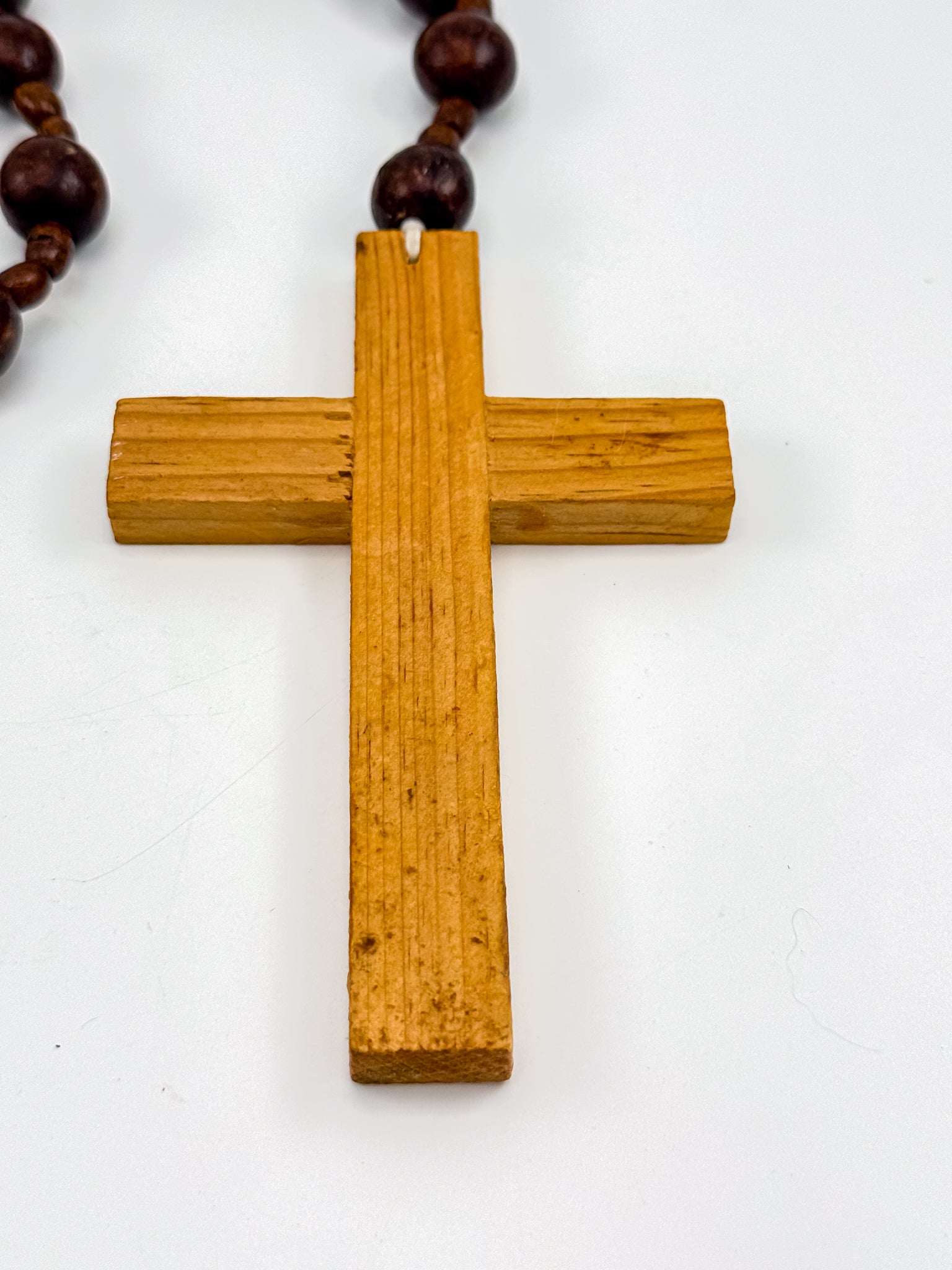 Vintage wood bead rosary coiled on white background showing deep burgundy beads and carved cross